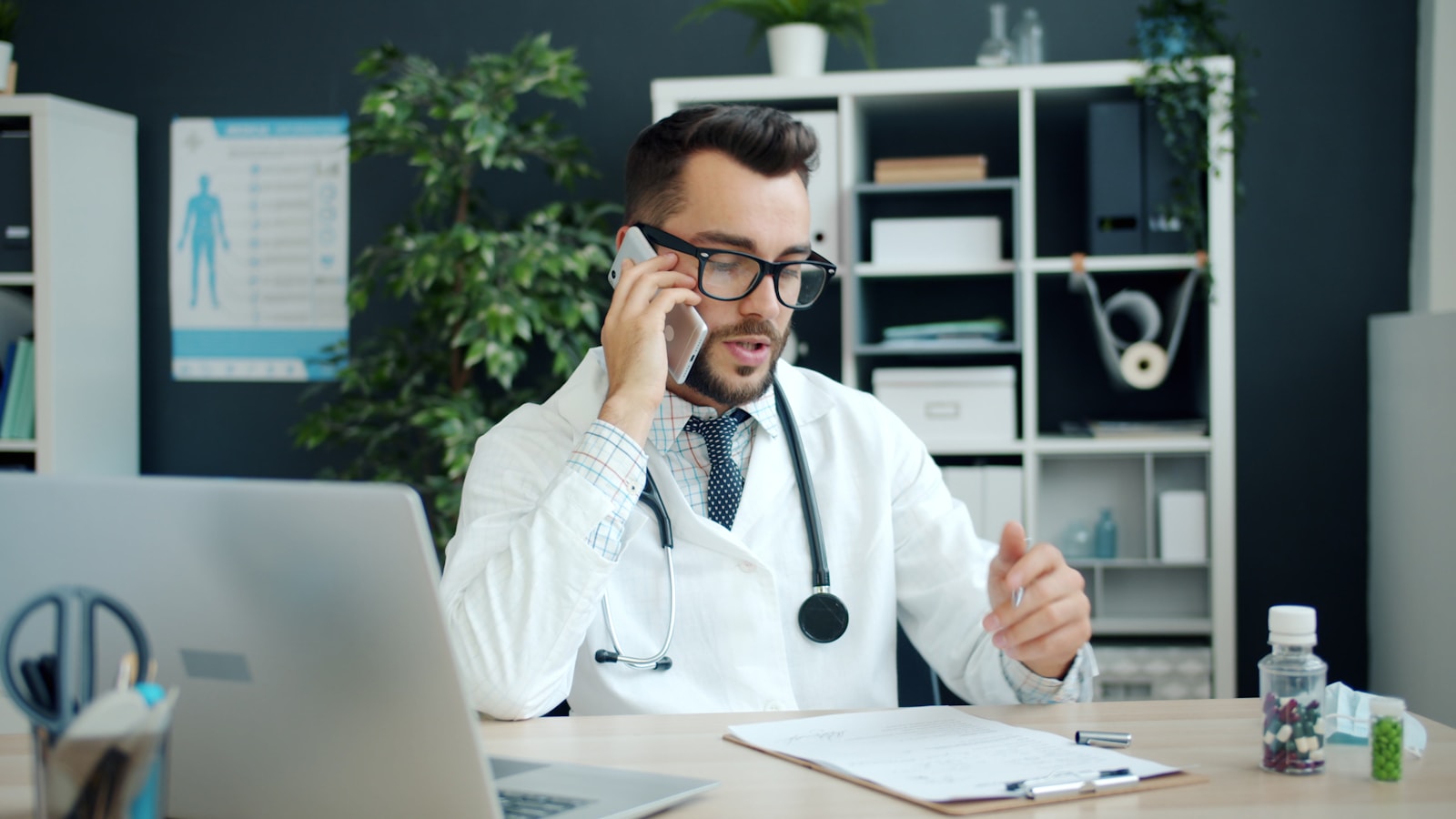 A physician in a white coat taking a telephone call at a clinical desk